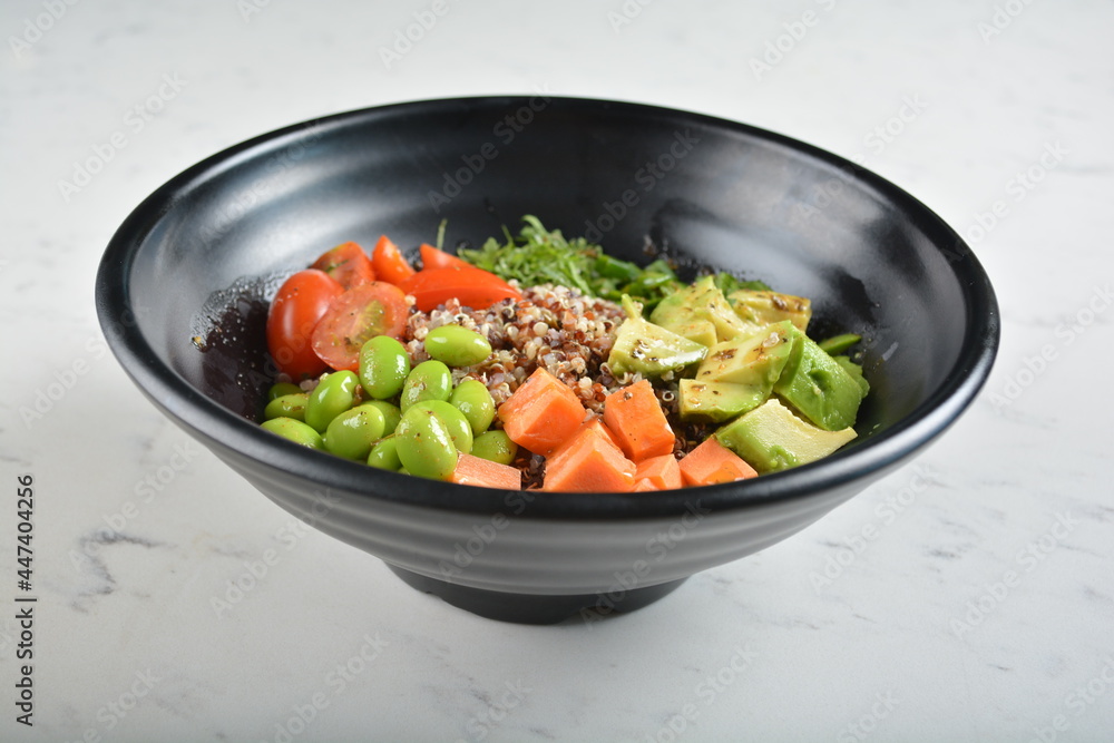 trio quinoa grain salad bowl with avocado, tomato, pea bean, carrot and brown rice in black bowl in white marble healthy poke bowl menu