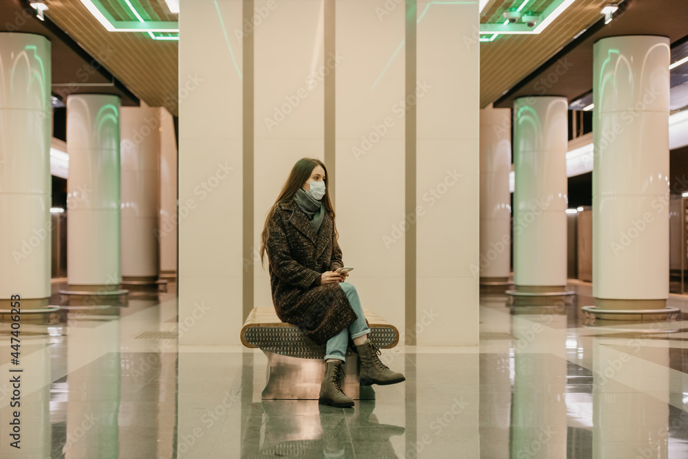 A woman in a medical face mask is waiting for a train and holding a smartphone. A woman in a medical face mask is waiting for a train and holding a smartphone.