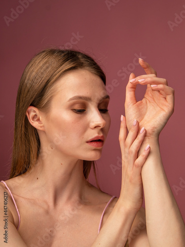 woman applying makeup on her face. Beautiful girl with bare shoulders, on a pink background. Woman with glowing skin