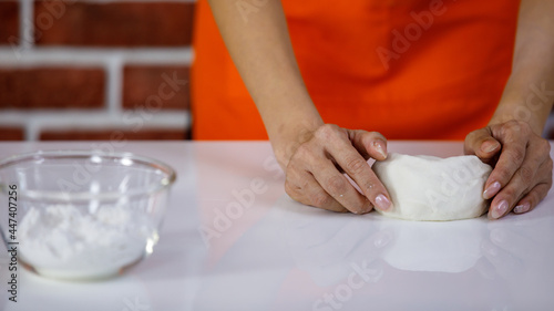 Chef in orange apron stand kneading mixing circle shape flour by hands on kitchen table when making dough use for baking cake croissant cookie and donut recipe