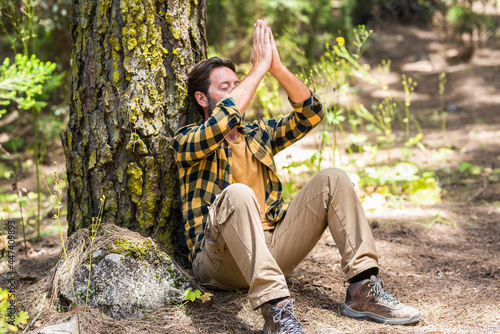Adult man in the forest sitting on the ground doing meditation and feel in love with woods outdoors nature around - concept of healthy lifestyle and happy peaceful people