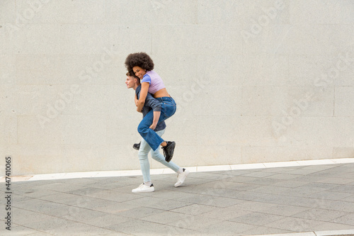 Caucasian young man carrying afro woman on his back having fun