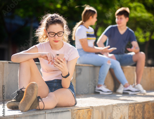 Teen girl playing on smartphone while sitting next to friends