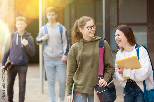 Two cheerful carefree female students walking down the street