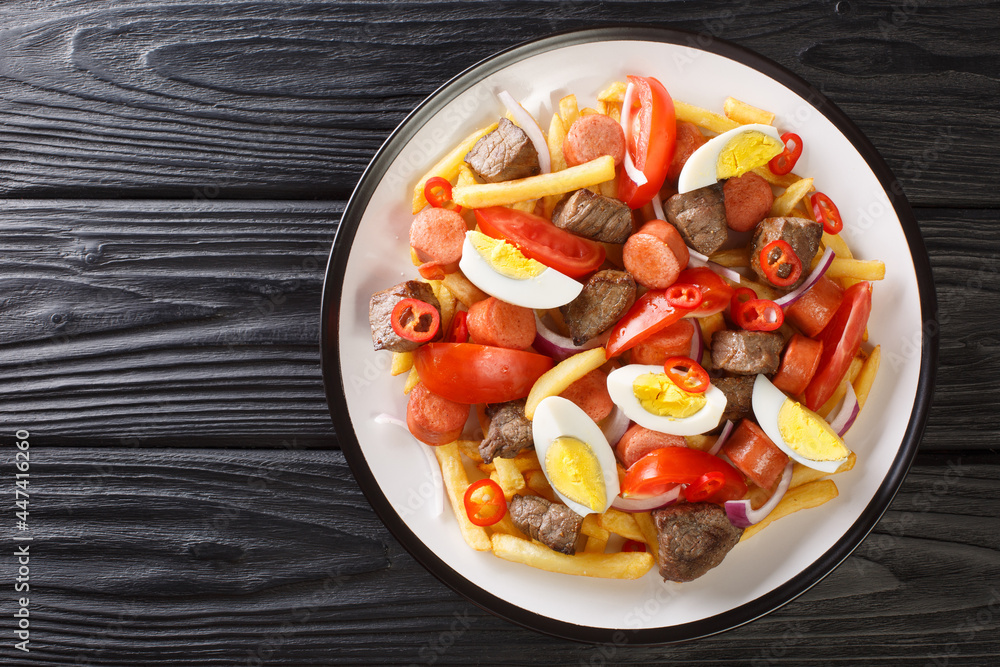 Pique macho is a Bolivian dish consisting of a layer of french fries buried underneath a heap of chopped beef, sausages, eggs, tomato, onions, peppers closeup in the plate. Horizontal top view Pique macho is a Bolivian dish consisting of a layer of french fries buried underneath a heap of chopped beef, sausages, eggs, tomato, onions, peppers closeup in the plate. Horizontal top view