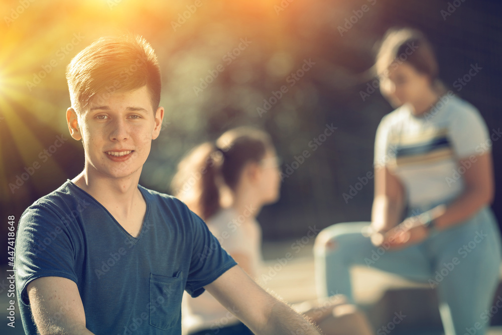 Fototapeta premium Portrait of cheerful teenager sitting on bench on city street, enjoying warm summer day