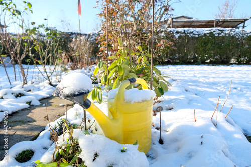 A yellow watering can stands in the snow-covered garden