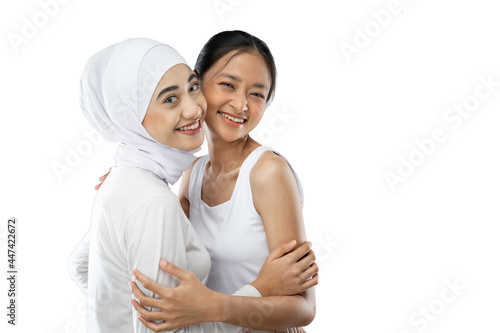 Smiling hijab girl and asian young girl bestfriend in front of camera with copy space against gray background