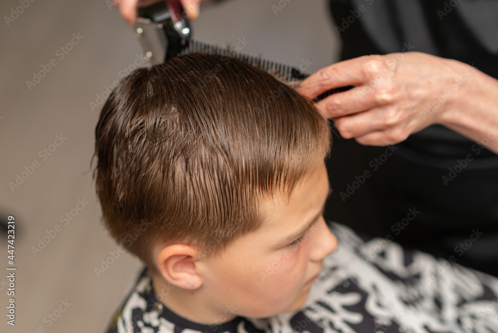 Cutting hair for young boy in a beauty salon.Hairdresser's hands holding a comb and a colorful scissors.Closeup. Cutting hair for young boy in a beauty salon.Hairdresser's hands holding a comb and a colorful scissors.Closeup.