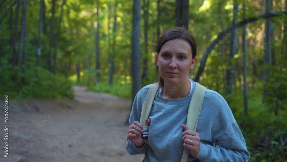 Portrait of Young Woman Tourist Among Green Forest, Looks Into The Camera. Concept of Hiking and Active Lifestyle Portrait of Young Woman Tourist Among Green Forest, Looks Into The Camera. Concept of Hiking and Active Lifestyle