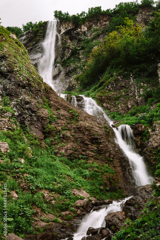 Beautiful mountain waterfall among trees, summer natural background, vertical photo