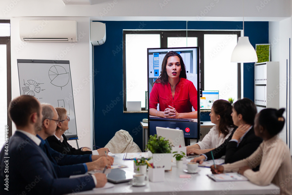 Diverse team of coworkers talking with project manager using webcam during business conference sitting in broadroom. Business people talking to webcam, do online conference participate internet Diverse team of coworkers talking with project manager using webcam during business conference sitting in broadroom. Business people talking to webcam, do online conference participate internet