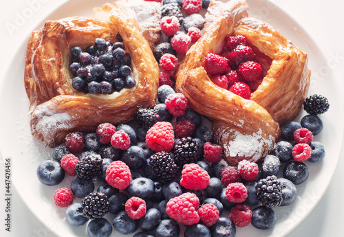 Danish with raspberries and blueberries on round plate with berries on white table