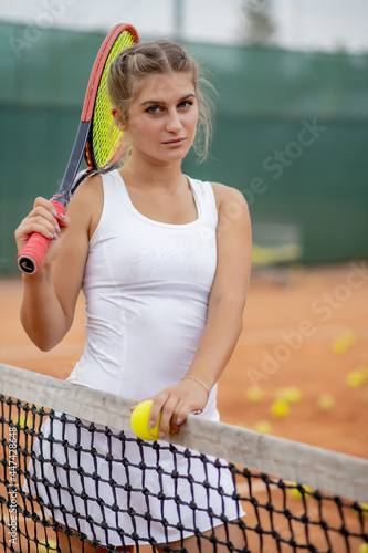 Athletic woman standing near net on court with racket in hands © volody10