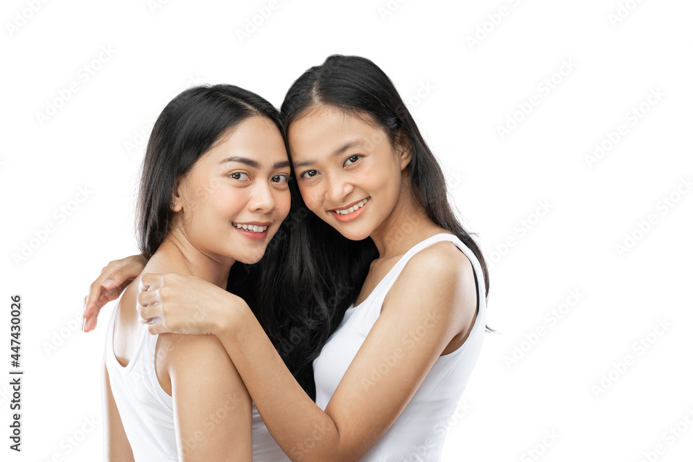 Two happy affectionate young woman hugging each other in a close embrace while laughing and smiling over gray background Two happy affectionate young woman hugging each other in a close embrace while laughing and smiling over gray background