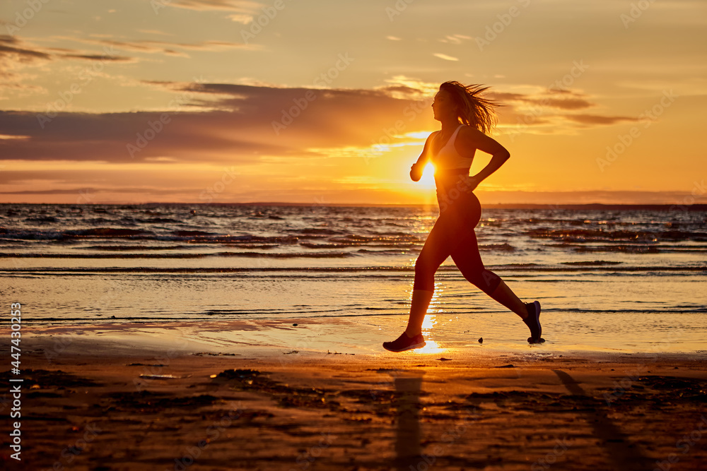Active lady runs near seaside on sand during sunset.