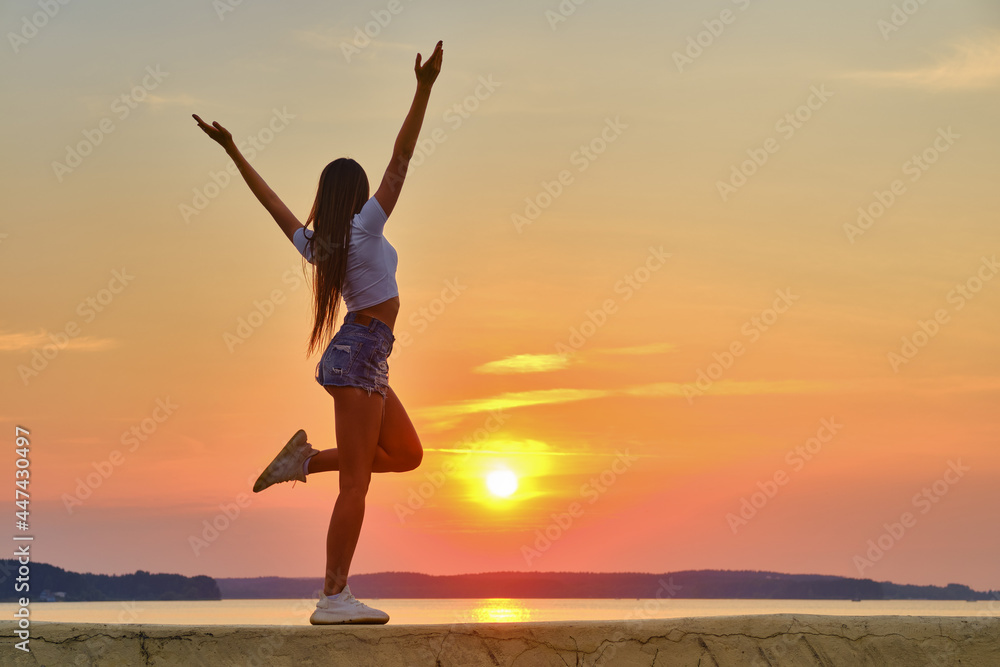 Young woman jumping and spreading hands to the sides and facing to the sunset Young woman jumping and spreading hands to the sides and facing to the sunset