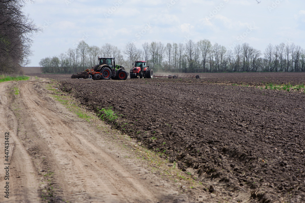 Fototapeta premium two red tractors, work in the field on a large tractor, harvesting, farming. two red tractors in a field in summer during an agricultural exhibition. Ukraine, Kiev region
