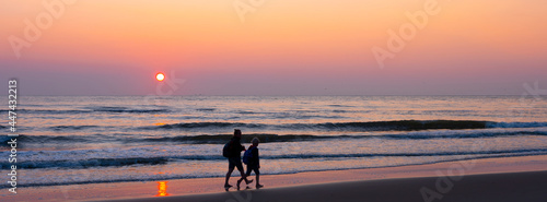 mother and child walk on beach during colorful sunset over north sea