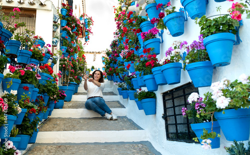 beautiful woman taking a selfie on a stairway full of pots and flowers in an Andalusian patio photo