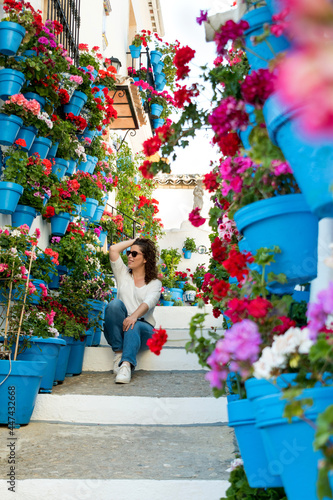 beautiful woman sitting on a ladder full of pots and flowers in an Andalusian patio photo