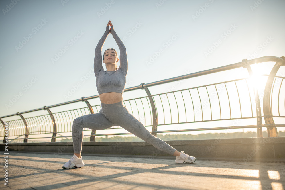 Cute girl in grey sportswear stretching her legs in lunges