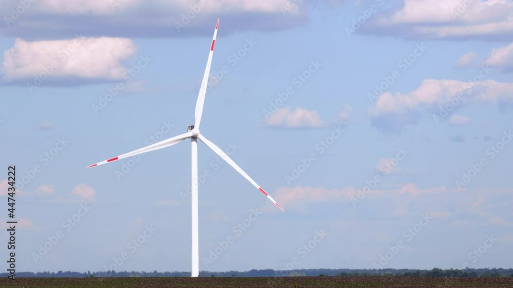 Rotating wind turbines at a distance in the field against the sky on sunny summer day Rotating wind turbines at a distance in the field against the sky on sunny summer day