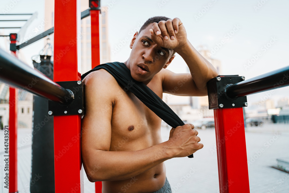 Black shirtless sportsman resting while working out on parallel bars