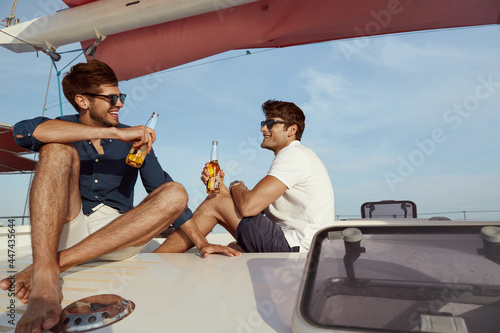 Foto Young male friends drinking beer on yacht in sea