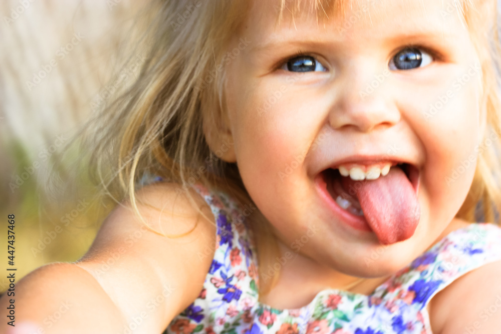 A funny infant 3 year happy old baby girl with open mouth and tongue out. Emotional portrait of a playful cheerful blonde-haired, blue-eyed beautiful girl. European child, smiling kid. Selective focus A funny infant 3 year happy old baby girl with open mouth and tongue out. Emotional portrait of a playful cheerful blonde-haired, blue-eyed beautiful girl. European child, smiling kid. Selective focus