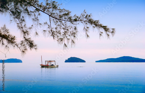 Beautiful sea scape with lonely traditional khmer boat, distant islands in morning mist, blue sky, blurred tree branch in Otres beach, Sihanouk ville, Gulf of Thailand, Cambodia, South East Asia photo