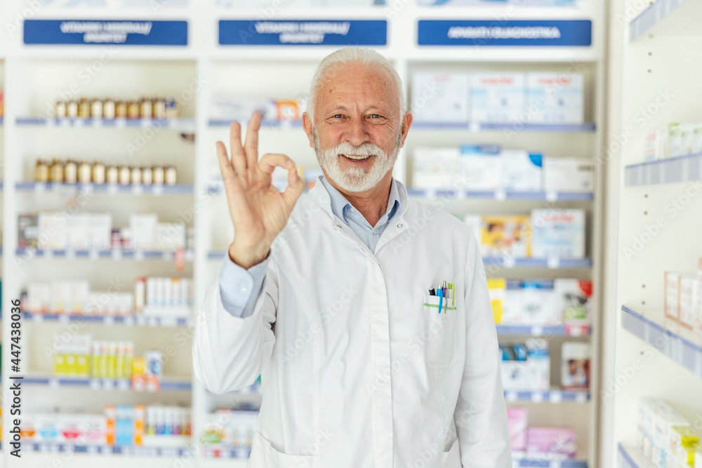 Portrait of a male pharmacist showing a sign of approval with his hand. A man with gray hair in a white uniform and gesturing approval with one hand. Look at the camera, smiling face