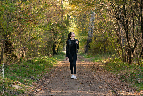 Beautiful girl walks in the autumn park. Young beautiful woman in black clothes in the forest. Alley, promenade. © somemeans