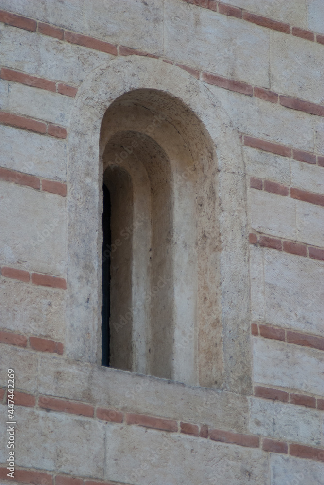 A close-up of a simple but stylish stone arched window set in the side of an Italian building