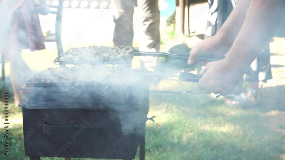Meat on the grill grid. An outdoor scene with a close-up view of man hands grilling meat at a private party in his home. Traditional homemade food grilling process - a view on the grate through smokes Meat on the grill grid. An outdoor scene with a close-up view of man hands grilling meat at a private party in his home. Traditional homemade food grilling process - a view on the grate through smokes