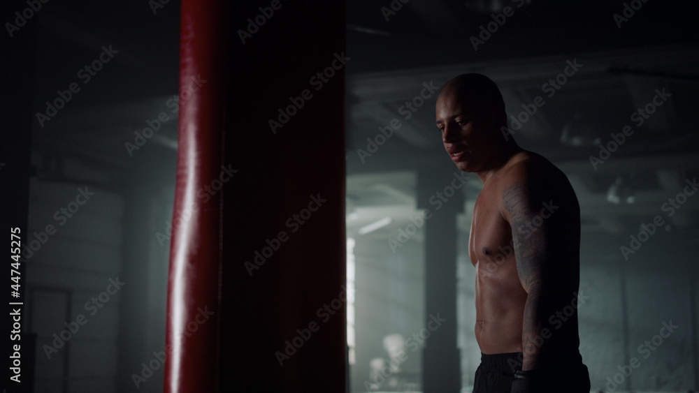 Athletic guy punching bag in sport club. Male boxer finishing strength exercise Athletic guy punching bag in sport club. Male boxer finishing strength exercise