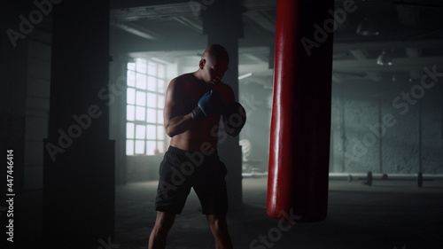 Boxer practicing kicks on punching bag in gym. Guy boxing sports bag in gloves © stockbusters