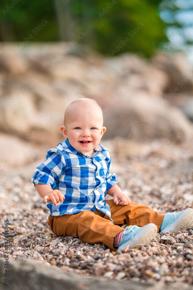 A little baby boy in a blue shirt plays with stones and shells on the beach A little baby boy in a blue shirt plays with stones and shells on the beach