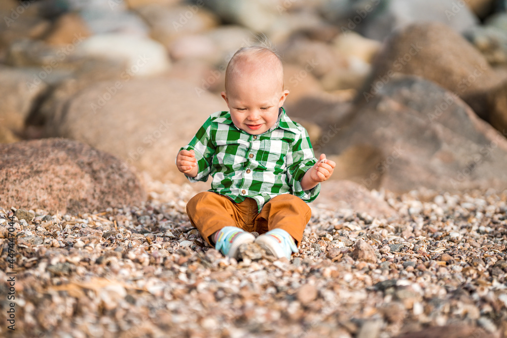 A little baby boy in a green shirt plays with stones and shells on the beach A little baby boy in a green shirt plays with stones and shells on the beach