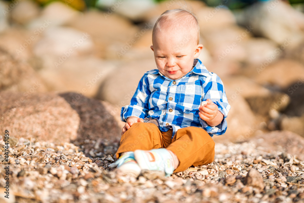 A little baby boy in a blue shirt plays with stones and shells on the beach A little baby boy in a blue shirt plays with stones and shells on the beach