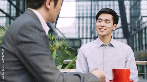 two asian men office workers meeting discussing business in outdoor cafe