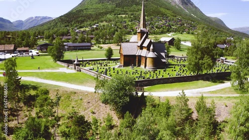 Exterior View Of Lom Stave Church Surrounded With Tombstone Near Village In Norway. - aerial tilt up photo