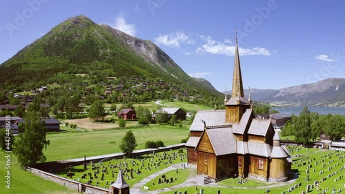 Lom Stave Church With Graveyard On A Sunny Day With Mountain Views In Lom, Innlandet County, Norway. - aerial photo
