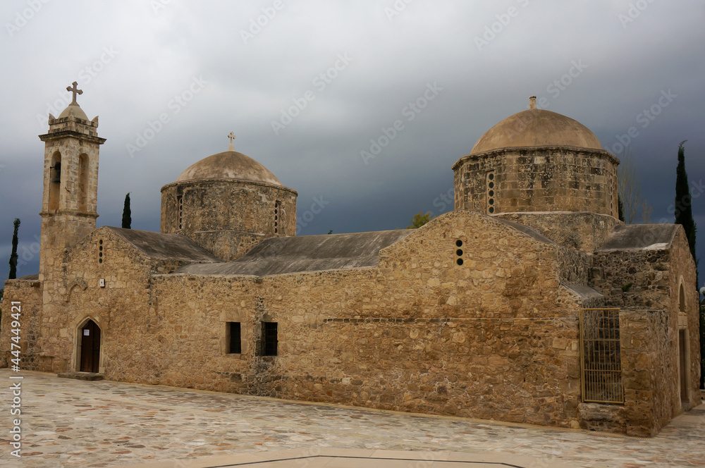 Panagia Chryseleousa Church in byzantine style, ancient stone-built structure with two domes and bell tower adorns the village square. Dark clouds gathering. Empa, Cyprus.