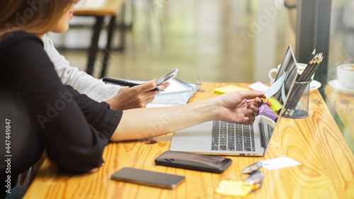 Two company workers talking about their to do list on sticky notes with laptop