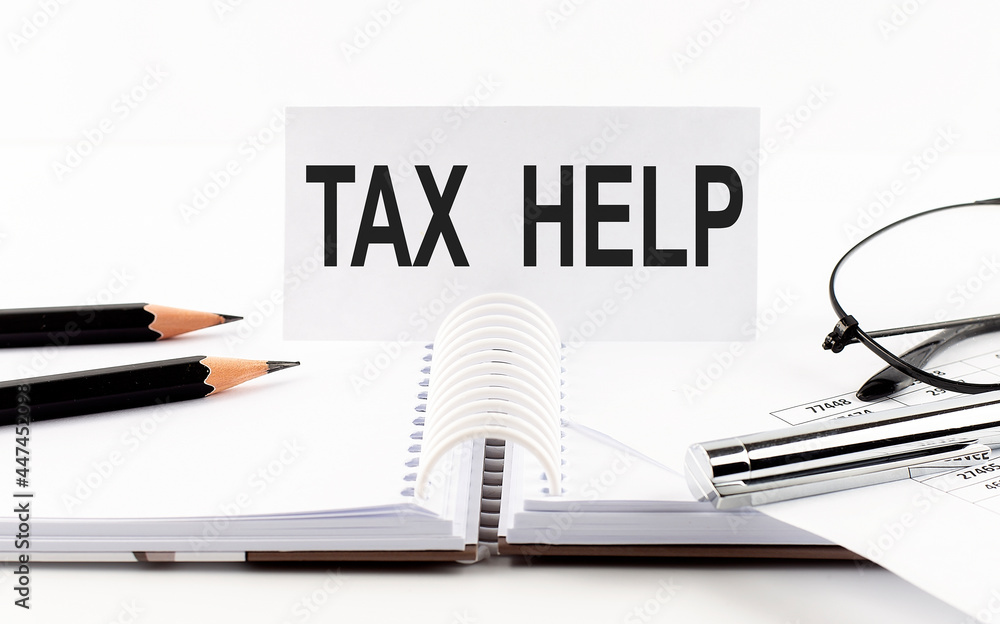 Text TAX HELP on paper card,pen, pencils, glasses,financial documentation on table - business concept Text TAX HELP on paper card,pen, pencils, glasses,financial documentation on table - business concept