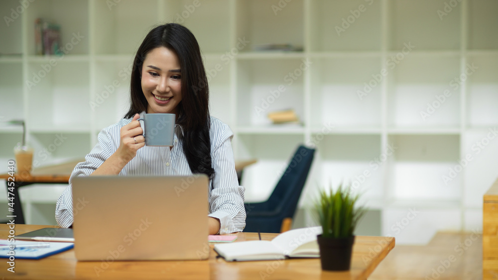 Beautiful marketing officer drinking coffee during working on laptop Beautiful marketing officer drinking coffee during working on laptop