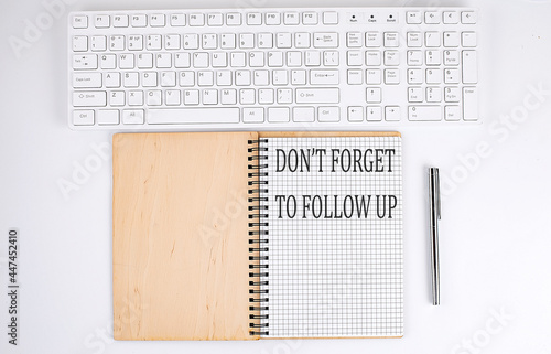 DON'T FORGET TO FOLLOW UP text on the notebook with keyboard on white background photo