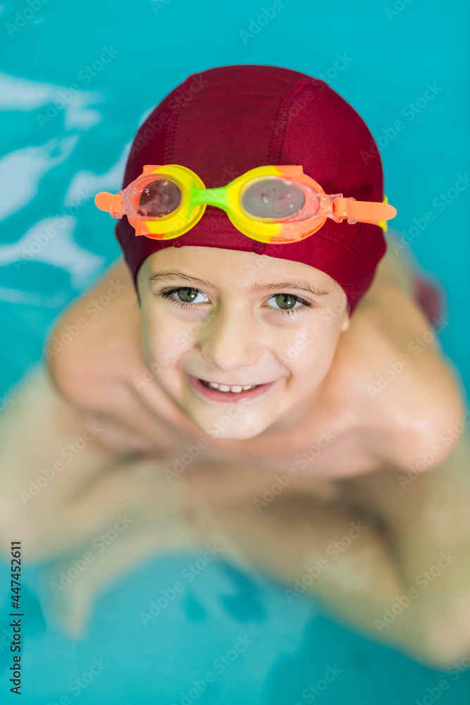 Portrait of a smiling child with a red swimming cap and water goggles.