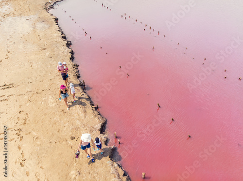 Aerial drone view tourist family group people walking along water edge shore coast of bright colorful pink salt lake on hot sunny summer day. Unusual travel destination and tourism concept photo